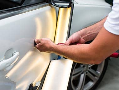 A mechanic is performing a Paintless Dent Removal process on a vehicle